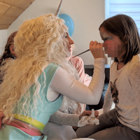 Kinderanimateurin schminkt ein Kind zur Einhornparty