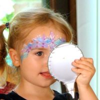 Ein geschminktes Mädchen bewundert sich im Spiegel, nachdem es von Kinderschminkerin in Rödinghausen geschminkt wurde.